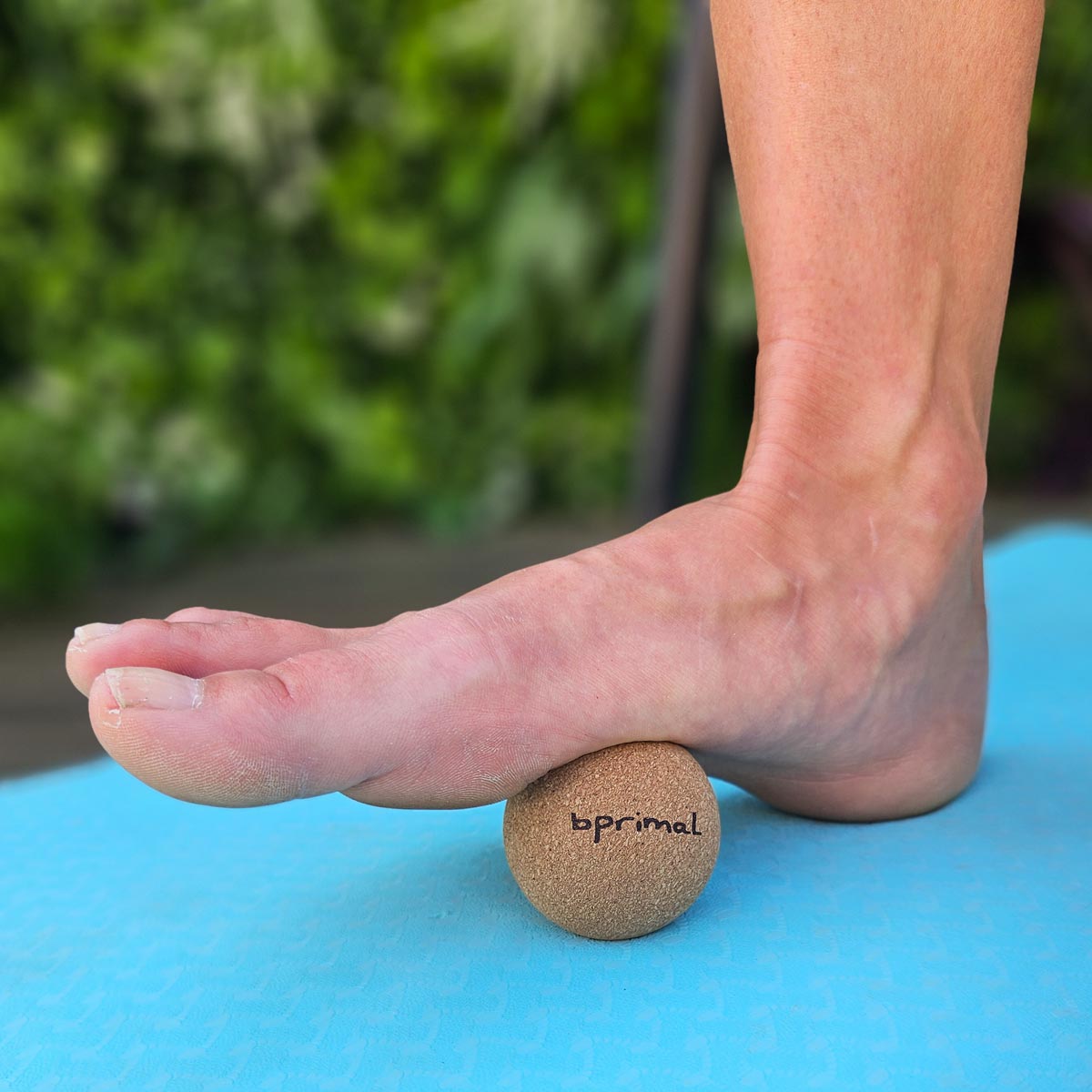 Person standing on a Bprimal Cork massage ball on a blue mat with a blurred green background