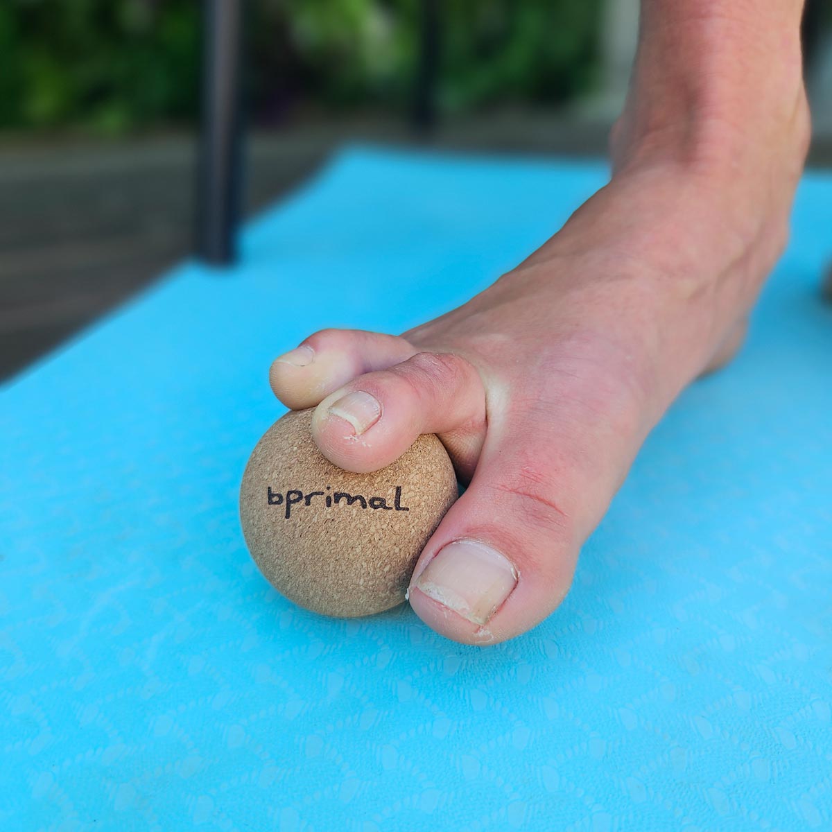 Foot with toes grasping a Bprimal Cork massage ball on a blue mat