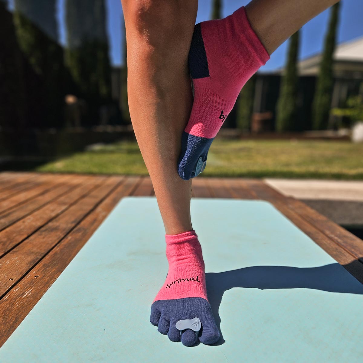 Person wearing Correct Toes - Stable Toe over pink and blue bprimal toe socks standing on a yoga mat outdoors