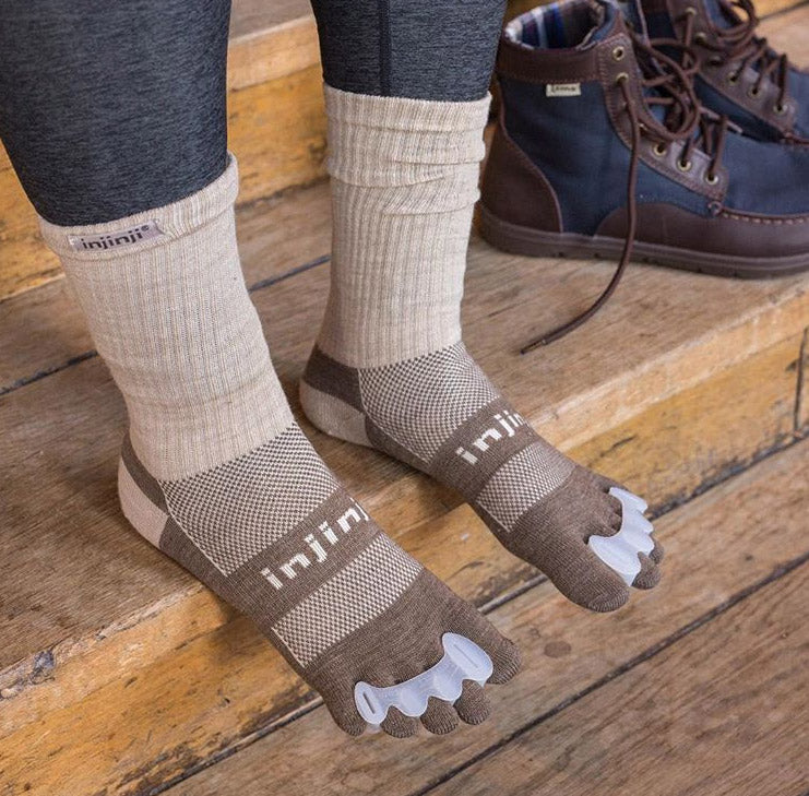Person wearing bprimal Correct Toes® - Toe Spacers over hiking socks, with hiking shoes in the background.
