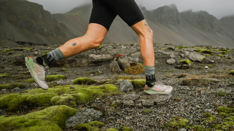 Altra Lone Peak 9+ Basalt men's running shoes on rocky trail terrain with runner mid-stride, showing grip and stability