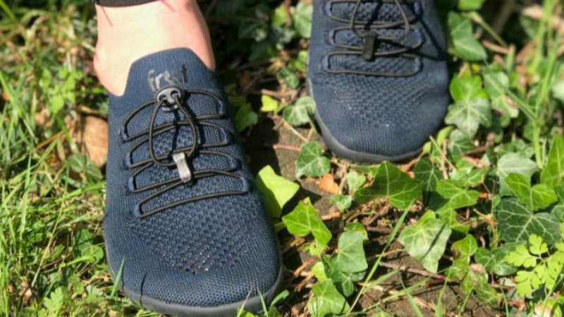 Person wearing dark blue Freet barefoot shoes with elastic quick-lace system standing on grass and green ivy.