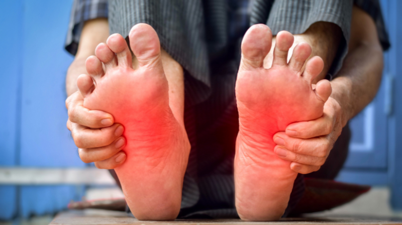 Person holding both feet with red highlighted soles illustrating neuropathy-related foot pain and sensitivity.