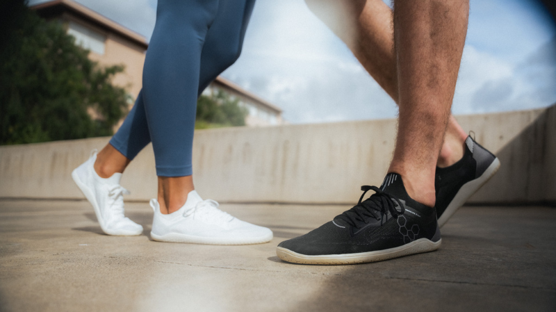 Two people standing outside on concrete surface wearing Vivobarefoot shoes in Australia with activewear. 