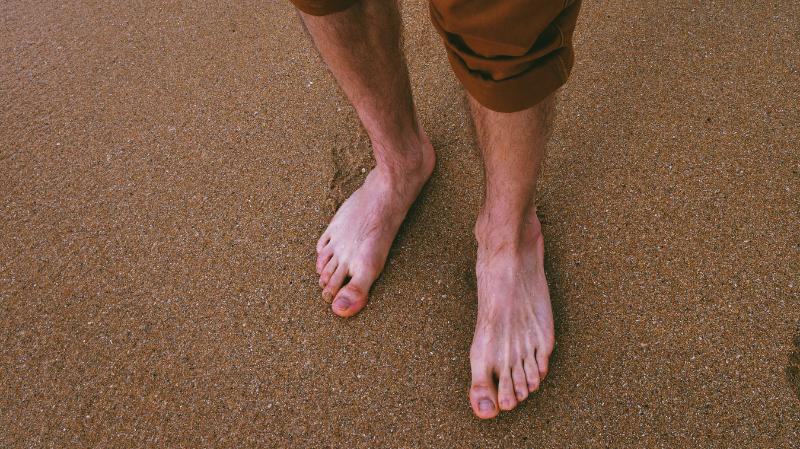 man walking barefoot on sand - natural foot pain relief