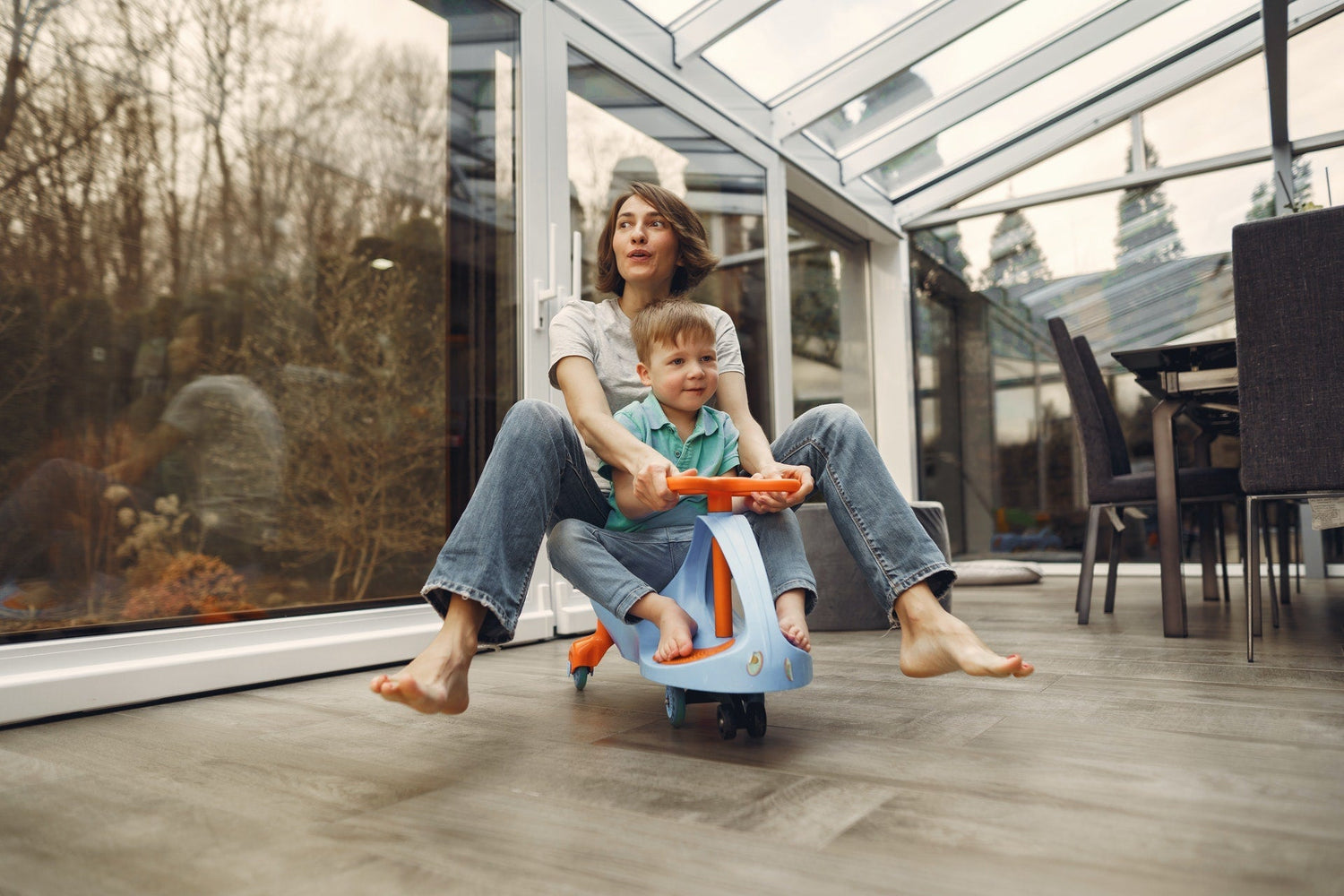 Mother and child riding a small toy indoors while barefoot, highlighting natural foot movement and family activity.