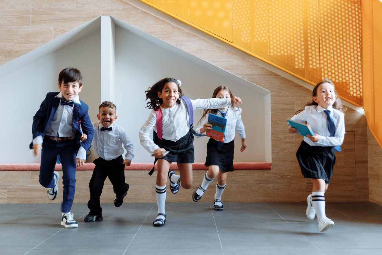 Group of school children running and playing together inside a modern school building hallway.