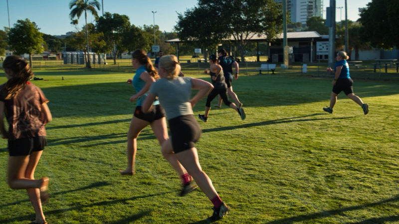 Runners practising barefoot running on a grassy Melbourne park field.