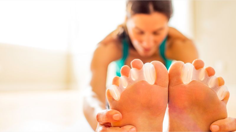 Person stretching while wearing Correct Toes toe spacers to improve toe alignment and natural foot function
