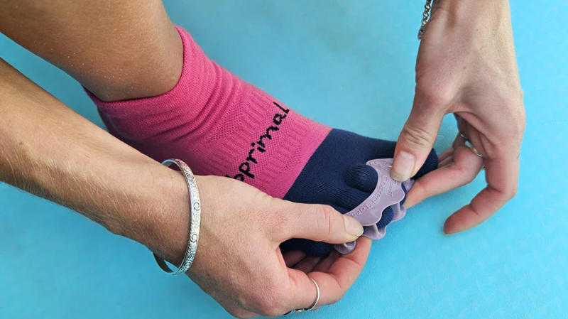 Person fitting Correct Toes silicone toe spacers over the toes while wearing Bprimal toe socks, demonstrating how toe spacers and toe socks can be used together to support natural toe alignment.