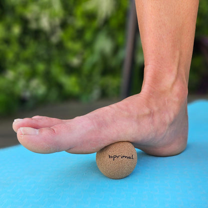 Person standing on a Bprimal Cork massage ball on a blue mat with a blurred green background