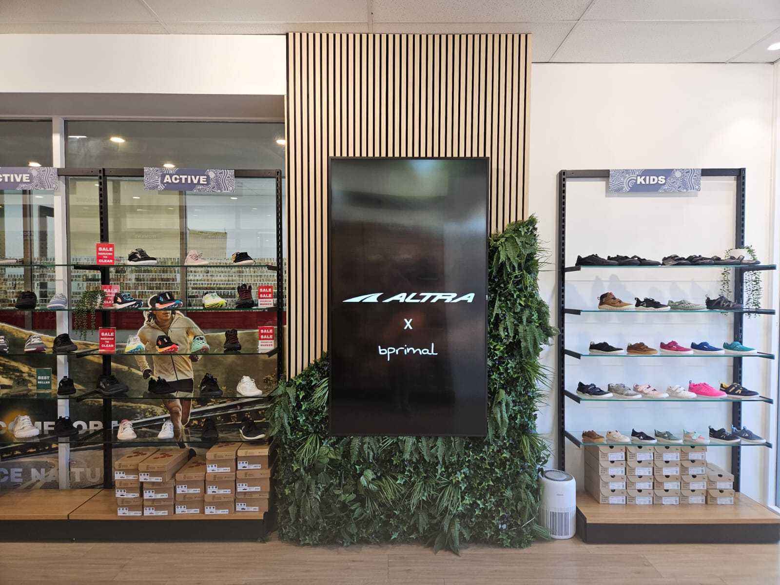 Bprimal Neutral Bay Store interior with a display of shoes and a large screen showing bprimal and Altra brand logos.